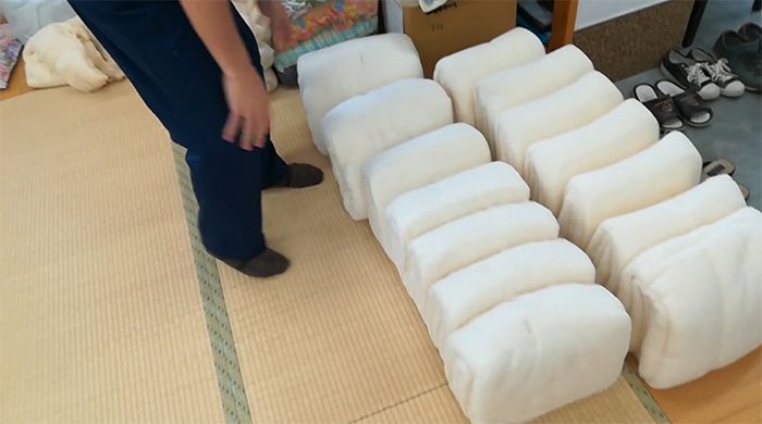 布団の製造工程「綿入れ」では1枚1枚折りたたまれた状態の綿を何枚もずらして重ねて折りたたんで敷布団の中身を完成させます。