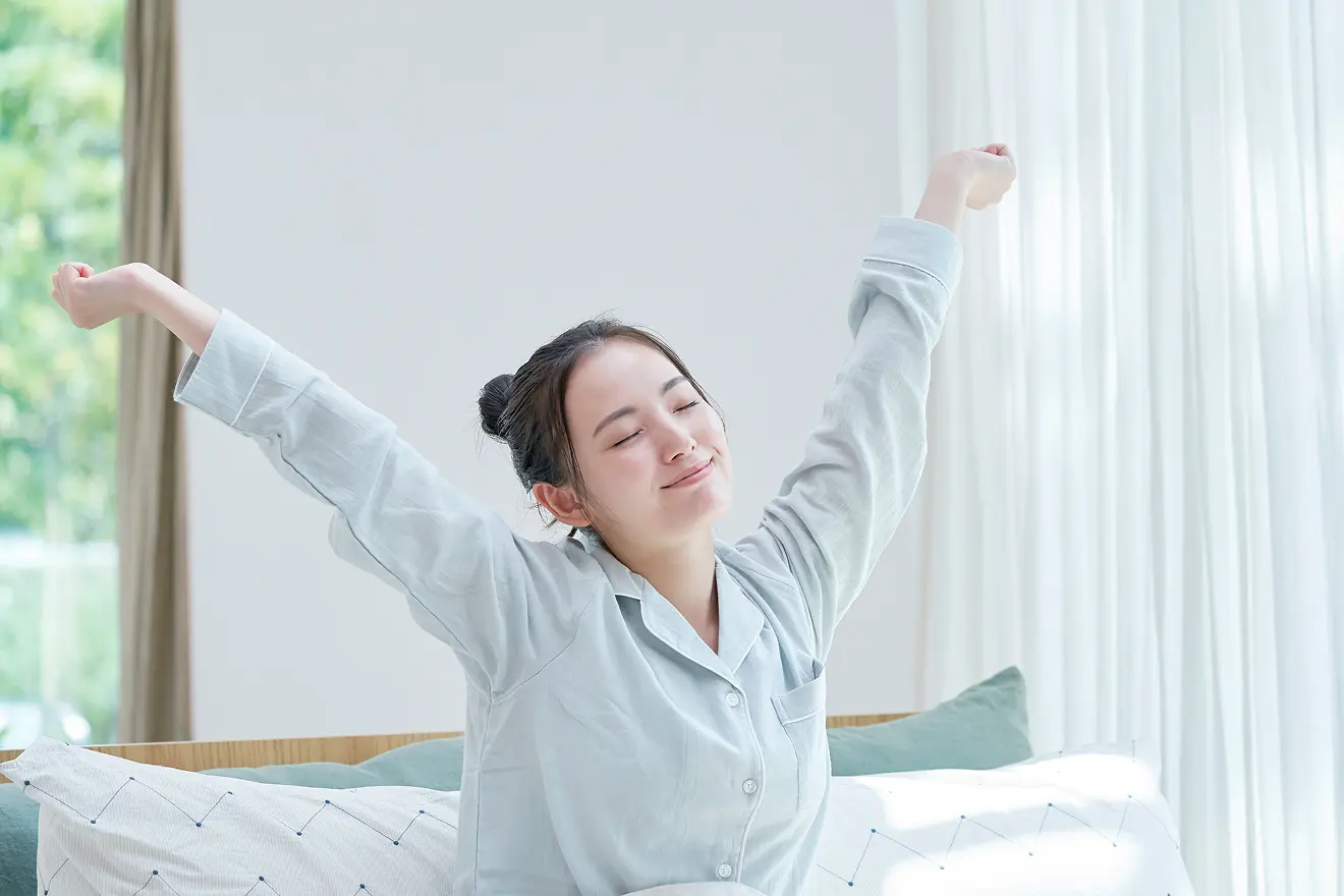 朝、日光を浴びながら起きる女性の写真