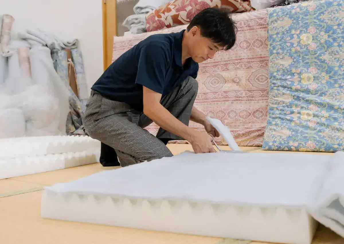 腰に負担のかかる姿勢で布団を作っている櫻道ふとん店代表 林 義浩 腰痛対策敷布団の「腰いい寝マットレスコレ1枚」を制作中の櫻道ふとん店代表 林 義浩
