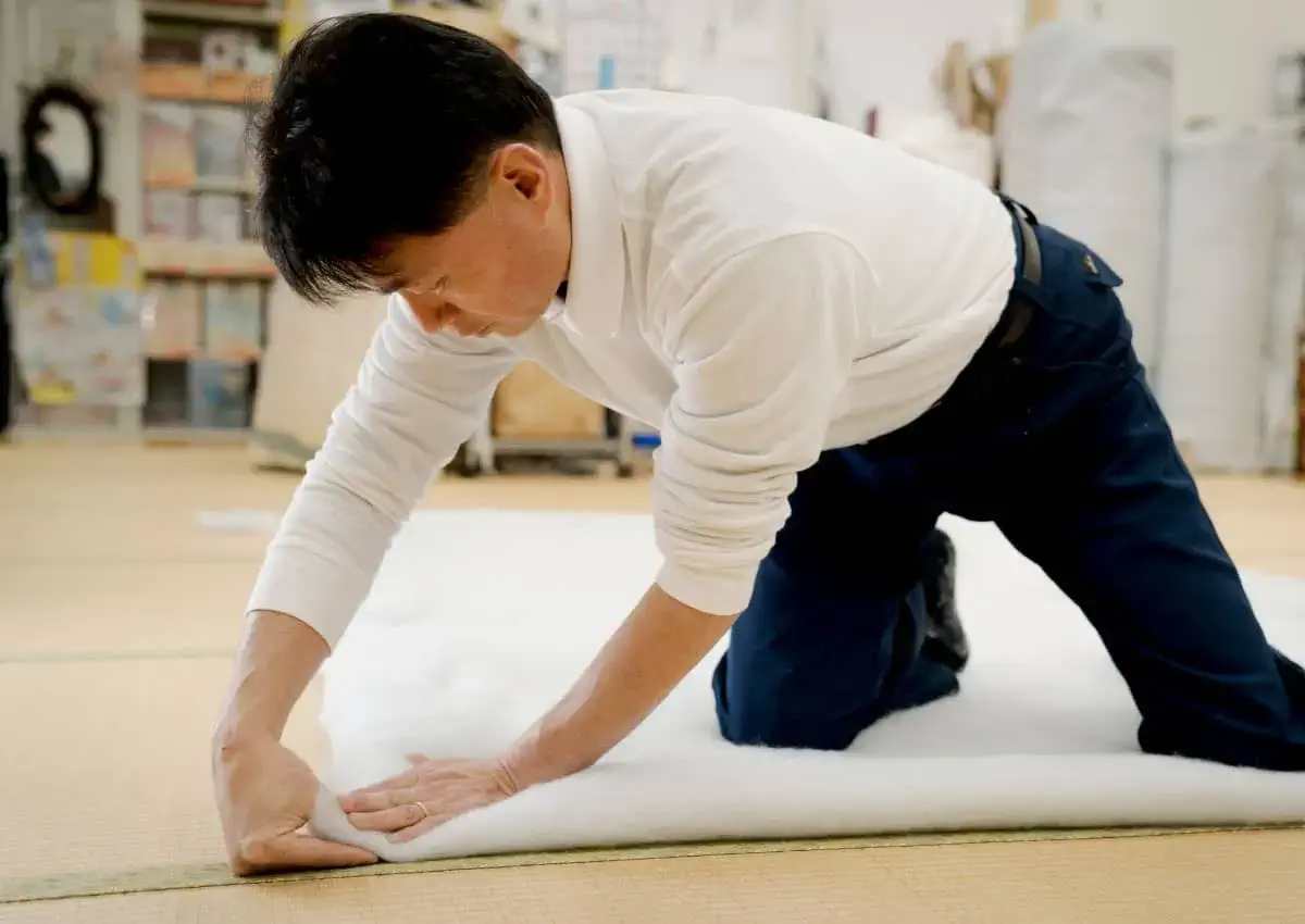 腰に負担のかかる姿勢で布団を作っている櫻道ふとん店代表 林 義浩